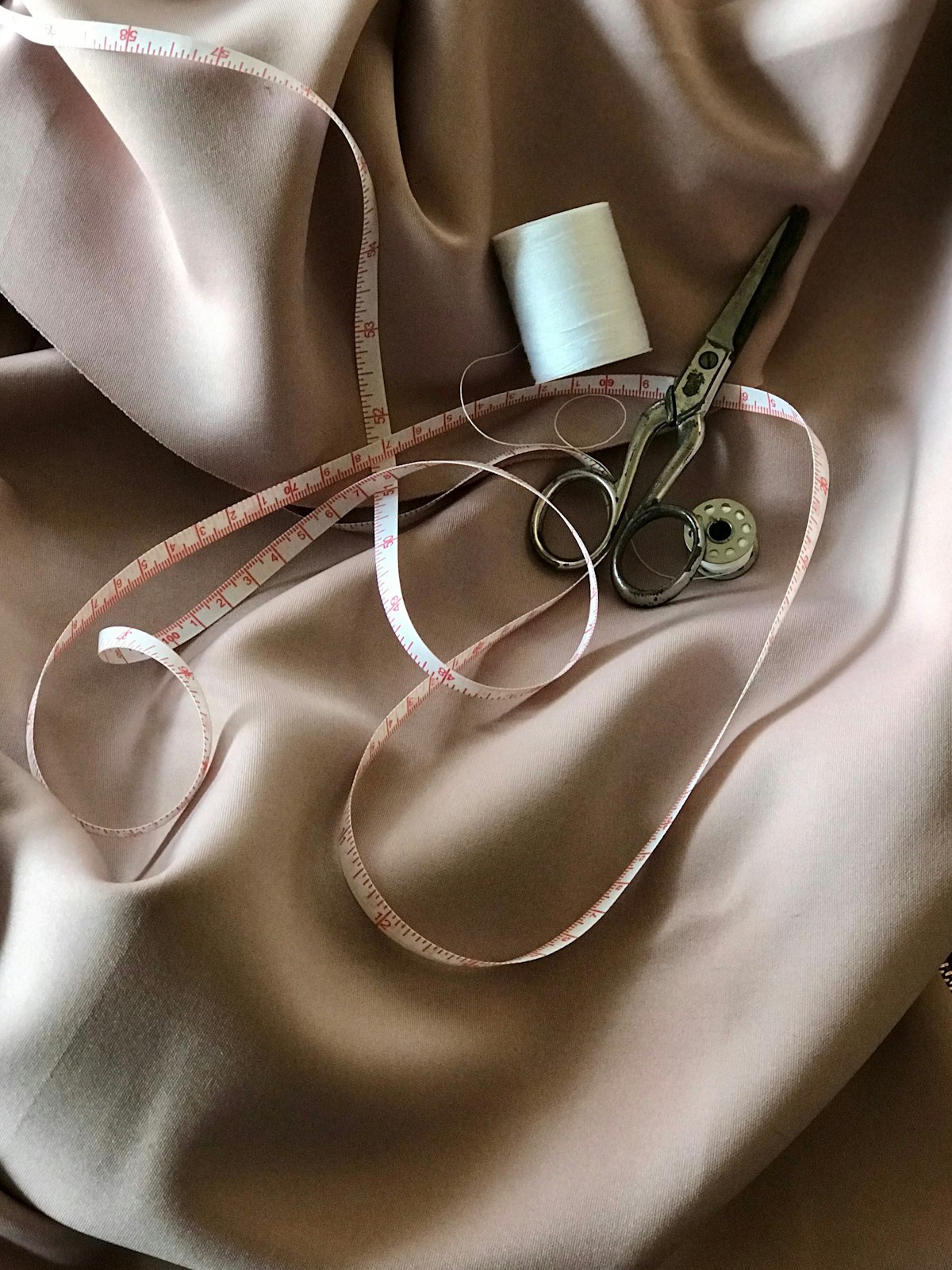 Measuring tape, scissors and thread laid across satin fabric