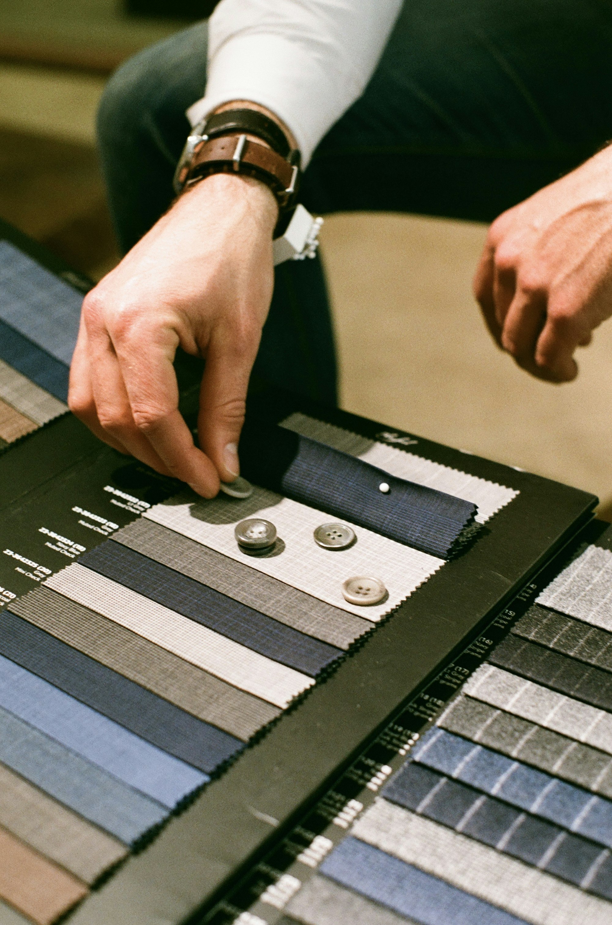 Fabric swatches, buttons and a tailor's hand selecting cloth